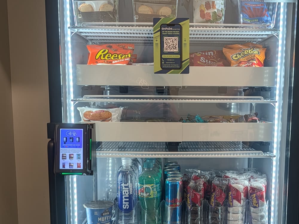 An On Point Amenities smart cooler with lit shelves, cashless reader, and fresh products